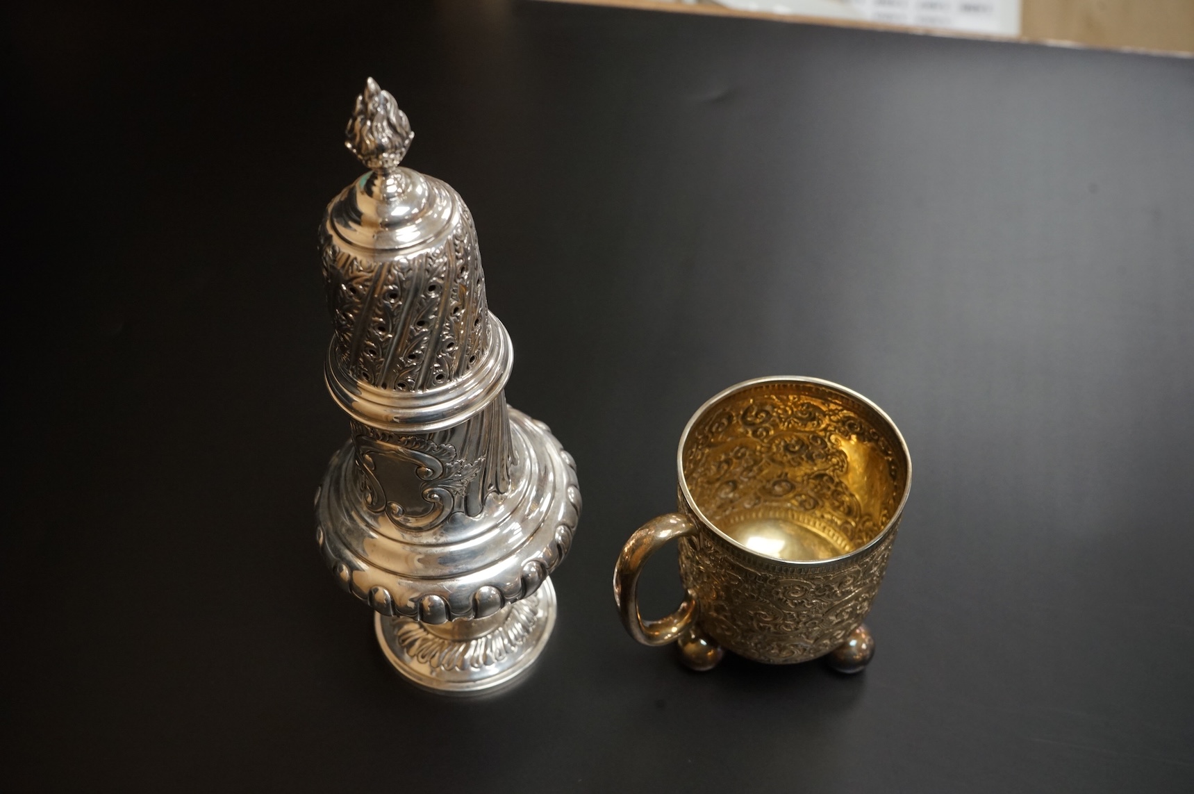 A Victorian embossed silver christening mug, on three ball feet, Martin, Hall & Co, London, 1874, height 85mm, together with a similar sugar caster, Lee & Wigful, Sheffield, 1899.